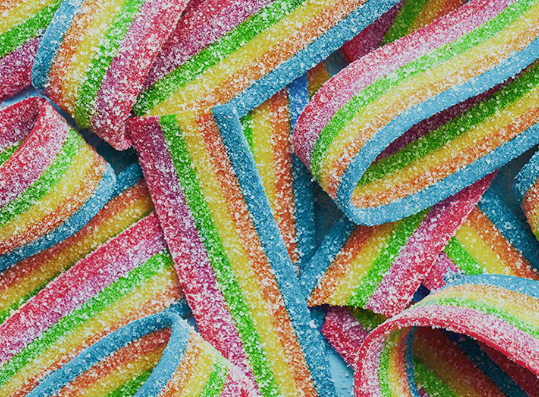 Macro top-down view of vibrant rainbow sour belts covered in sugar crystals, used as a grounding tool for anxiety relief.