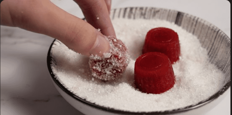 What makes sour candy sour: A red gummy being rolled in citric acid and sugar.